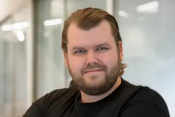 Portrait of a man with short brown hair and a beard wearing a black shirt, in a modern glass-walled office.